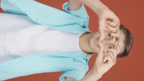 Vertical-video-of-Boy-making-heart-sign-at-camera.